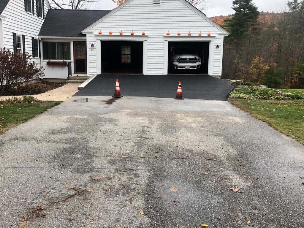 Curved driveway approach freshly sealed, deep black finish against green summer lawn
