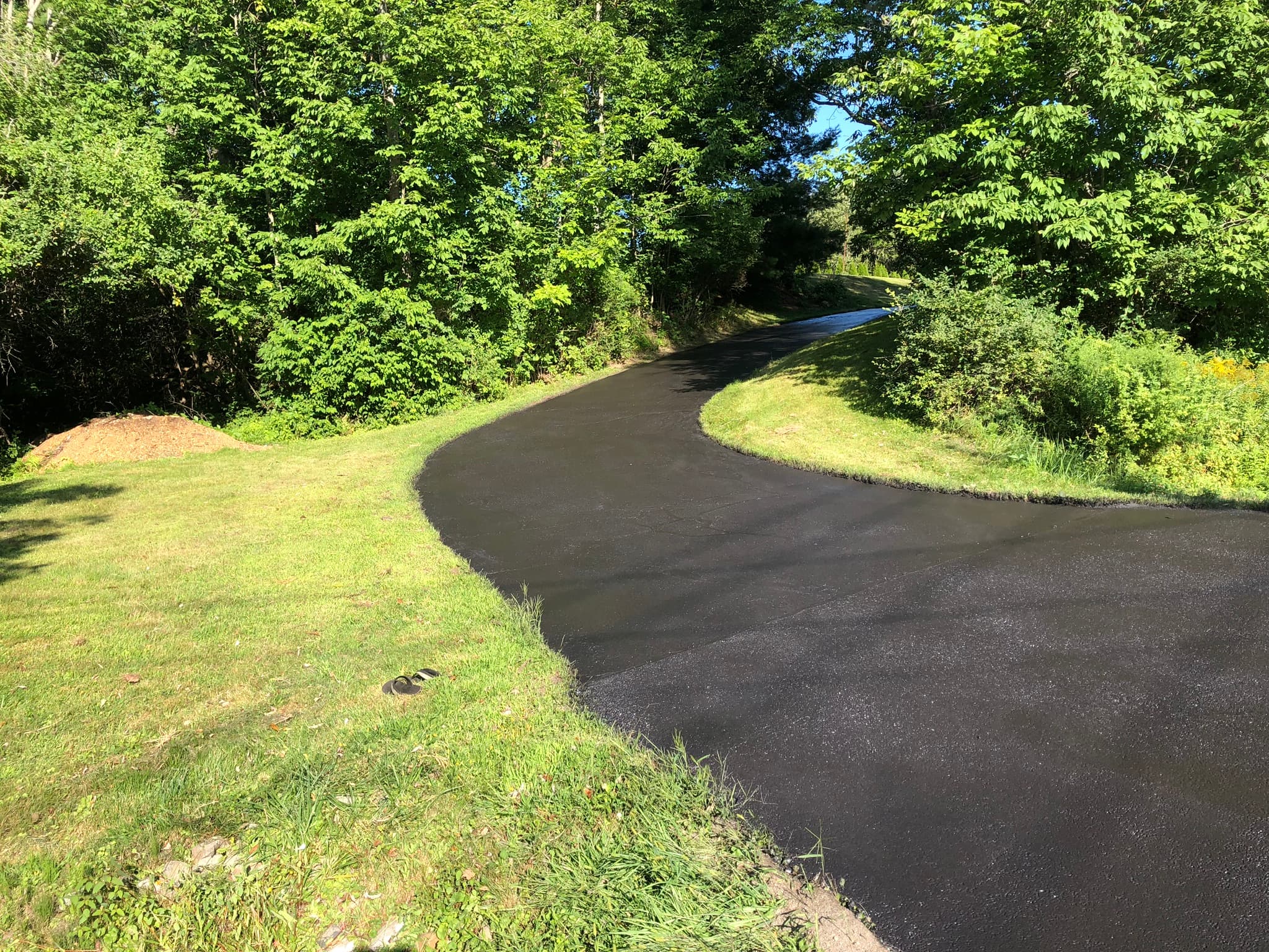Wide residential driveway with large lawn, fresh deep black finish, summer