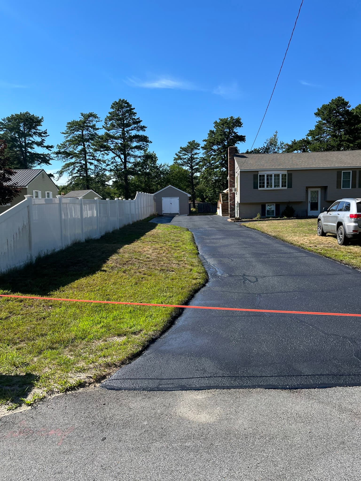 Colonial home with long driveway, freshly sealed, green summer lawn contrast