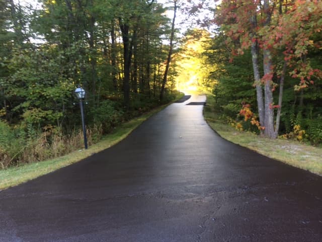 Stone-faced colonial home, pristine freshly sealed driveway with perfect edge work along stone wall