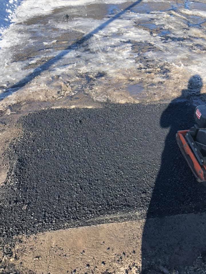 Hot-mix asphalt patch being compacted with a plate compactor, year-round repair work